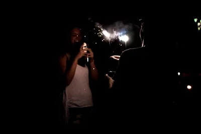 A person holds a sparkler while another takes a photo of them on a smartphone