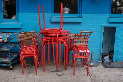 Stacks of chairs on sidewalk next to a restaraunt worker looking out from a basement doorway